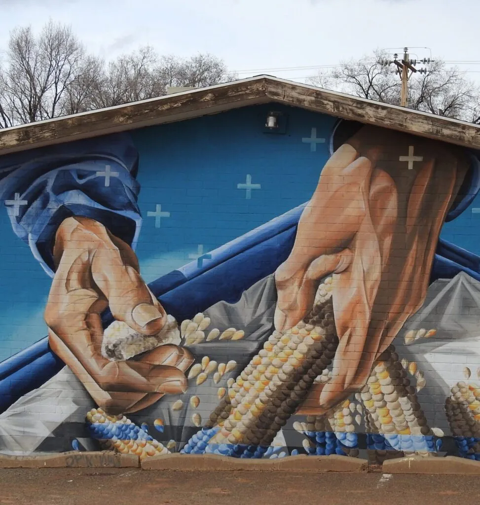 A mural depicts hands holding ears of colorful corn against a blue background.