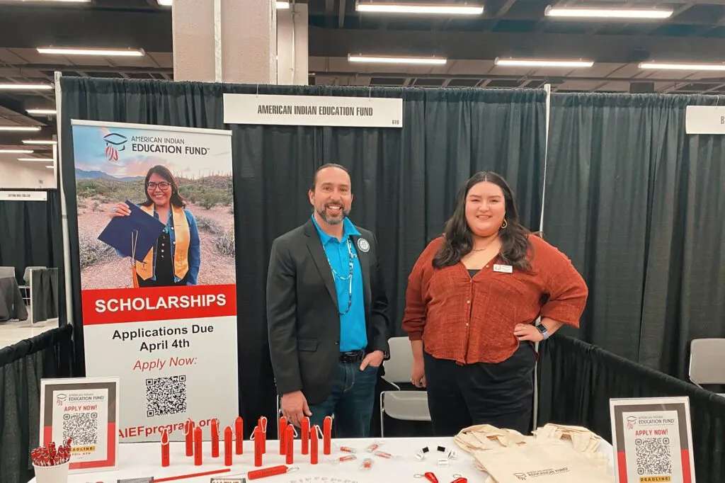 A booth for the American Indian Education Fund with two people, offering scholarship information.