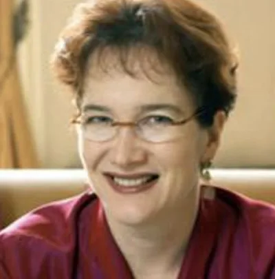 A person with glasses and short hair is smiling, wearing a red top.