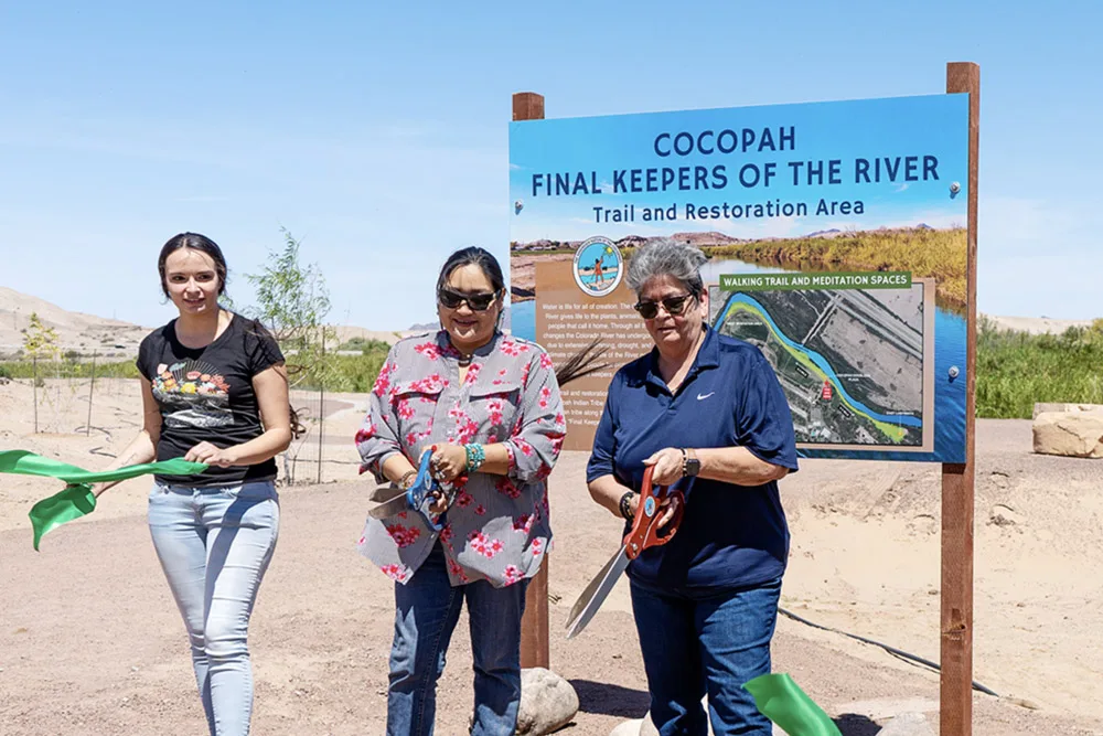 Three people holding a ribbon-cutting ceremony next to a sign for the Cocopah "Final Keepers of the River" trail.