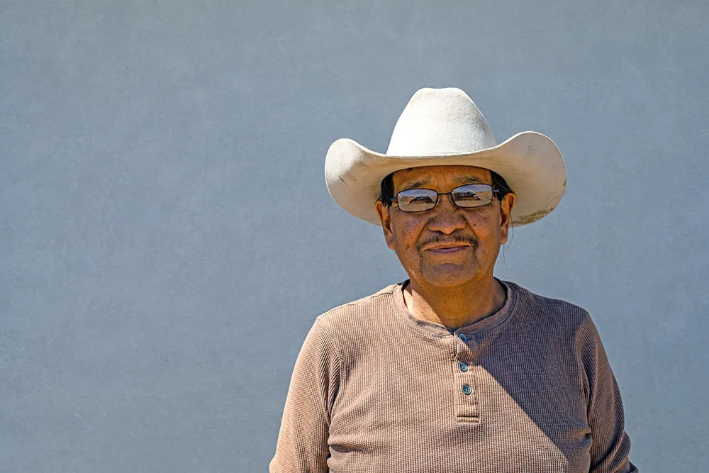 A man wearing a cowboy hat and glasses stands against a plain background.