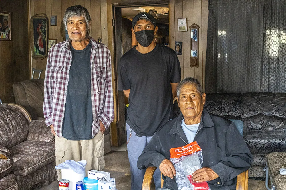 Three men are indoors with donation supplies like food and toiletries visible; possibly related to southwest reservation aid.