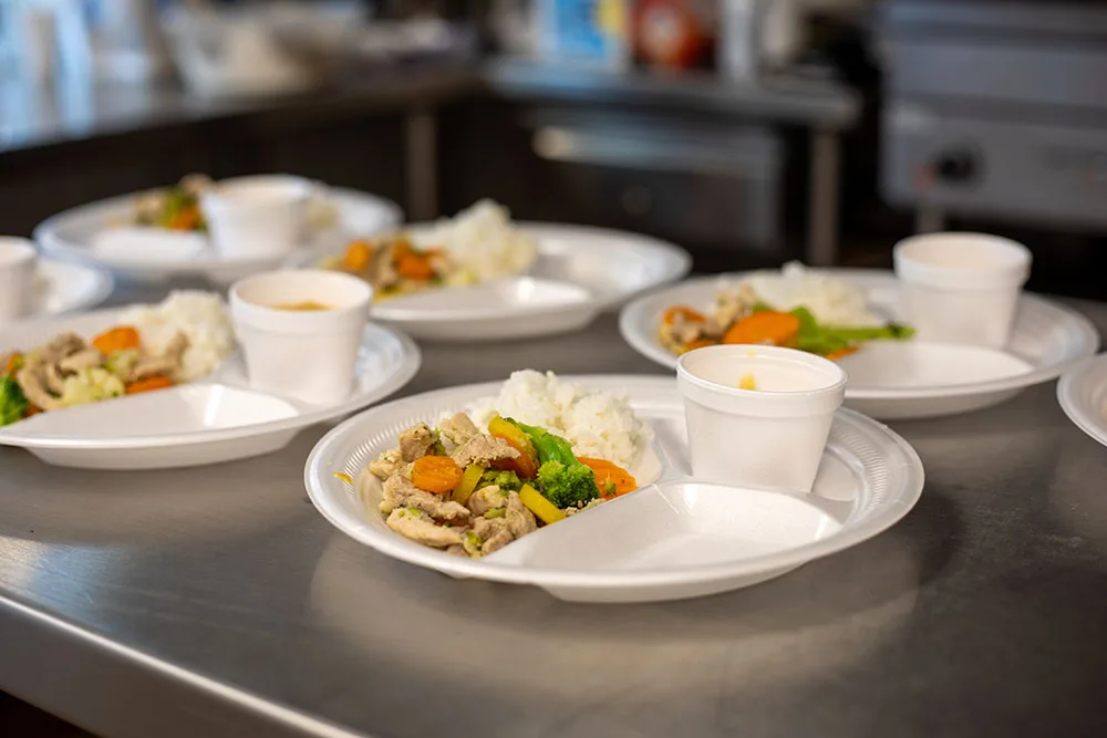 Disposable plates with a meal of rice, vegetables, and soup cups are arranged on a counter. Southwest reservation aid is not relevant.