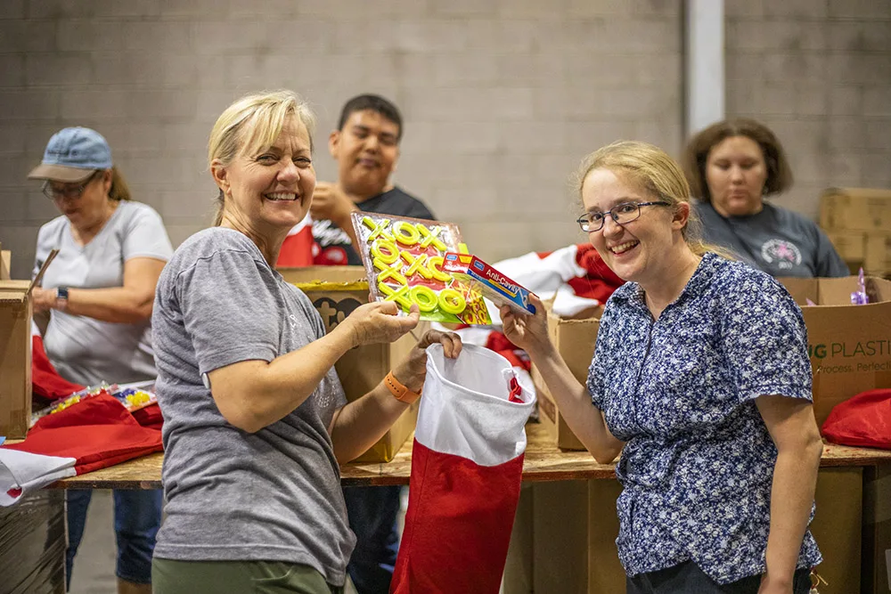 People are smiling and packing items into stockings, suggesting volunteer work. Southwest Reservation Aid might be relevant.