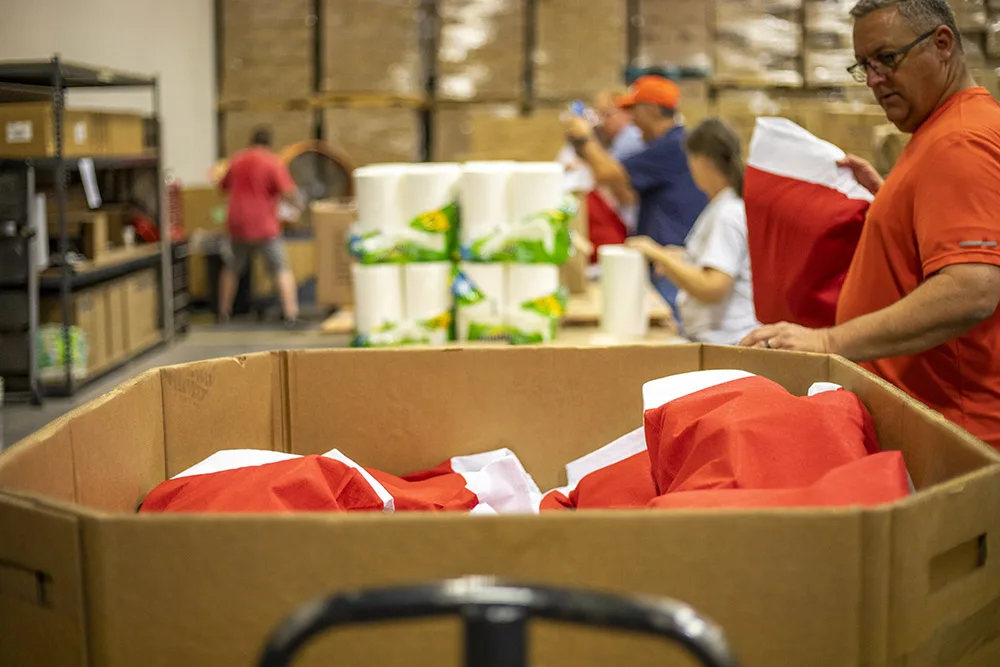 People are working in a warehouse with large boxes and red bags, possibly organizing supplies.