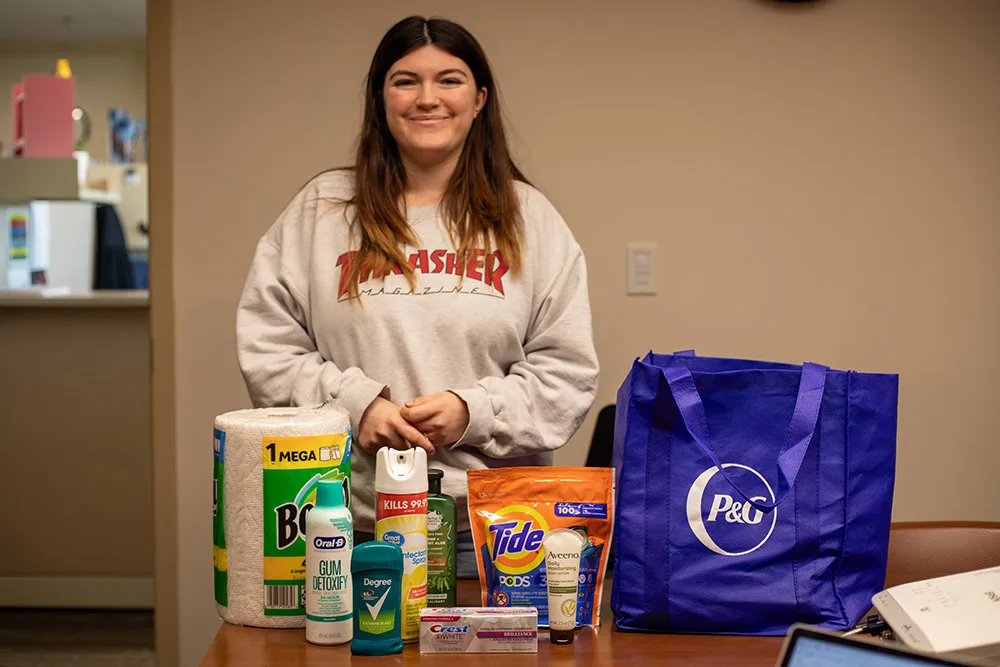 A person is standing behind various household items and a P&G branded bag on a table.
