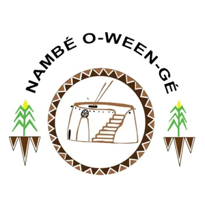 Logo featuring "Nambé O-Ween-Gé" with an adobe structure and corn motifs.