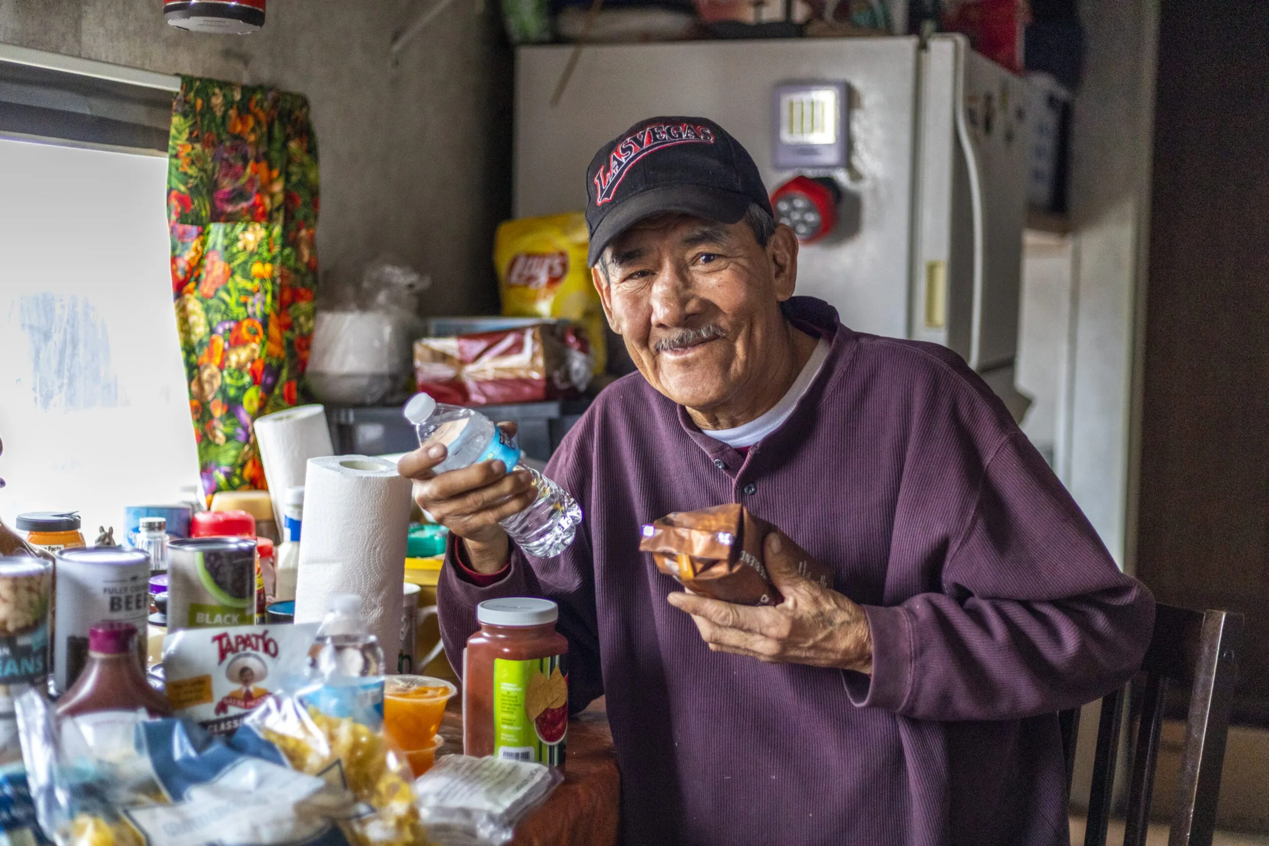 A person holds a water bottle and food in a kitchen filled with supplies. Navajo relief fund may be relevant.