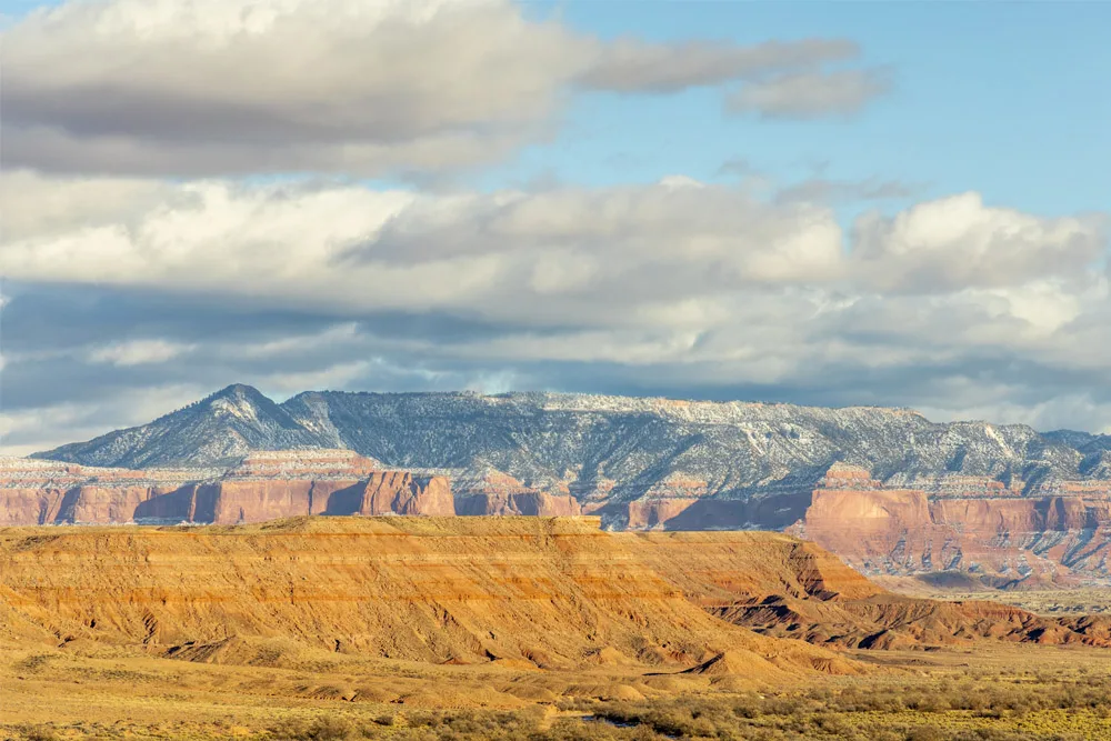 Desert landscape with mesas and distant mountains under a partly cloudy sky, possibly Arizona Navajo region.