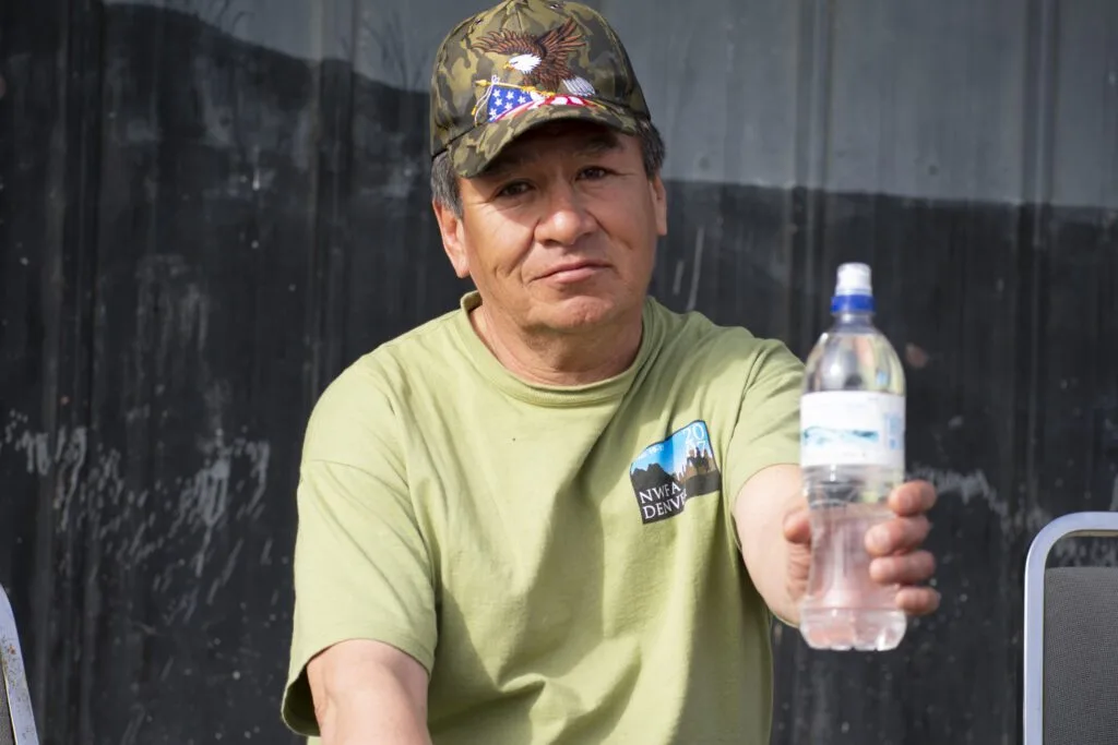 A person wearing a cap and green shirt is holding a water bottle.