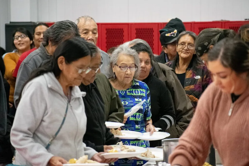 A group of people are gathered, likely at a community event, in a food line.