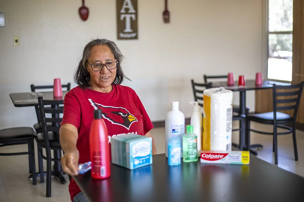 A person in a red shirt is sitting at a table with various hygiene products and a tissue box.