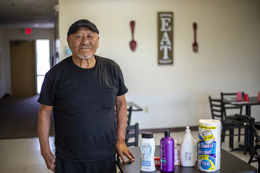 A man stands in a room with cleaning and hygiene products on a table.