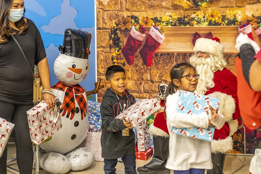 Children receive gifts from Santa, with holiday decorations, including a snowman.