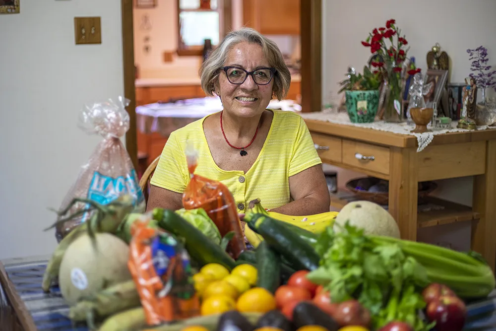 A woman sits at a table with a variety of fresh fruits and vegetables.