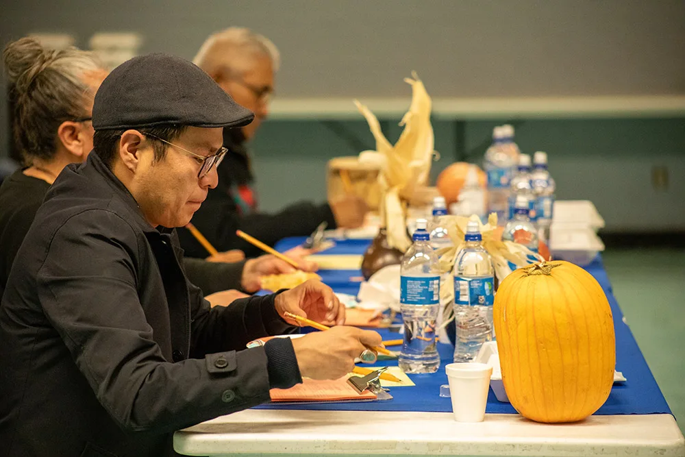 People are sitting at a table with food, drinks, and decorative pumpkins, engaged in conversation or dining.