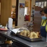 A person wearing a face mask and apron is preparing food in a kitchen.