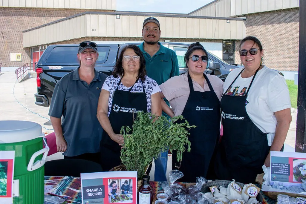 A group of people is standing at a booth promoting a native American nonprofit organization.