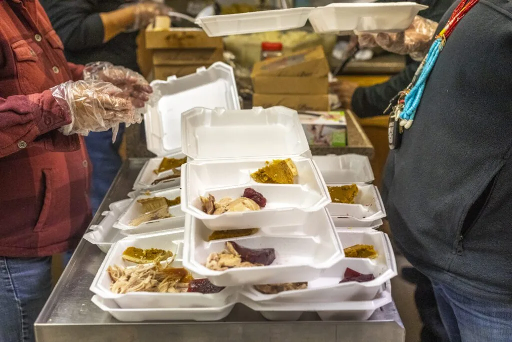 People are packing food into takeout containers, possibly for distribution by a relief effort, such as the Navajo Relief Fund.