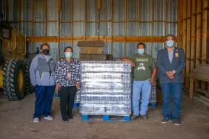 Four people stand in a warehouse next to a pallet of bottled water, all wearing masks. Navajo relief fund keyword is appropriate.