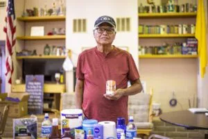 A person holds a can, surrounded by various supplies on a table. Shelves filled with books are in the background. Navajo relief fund.