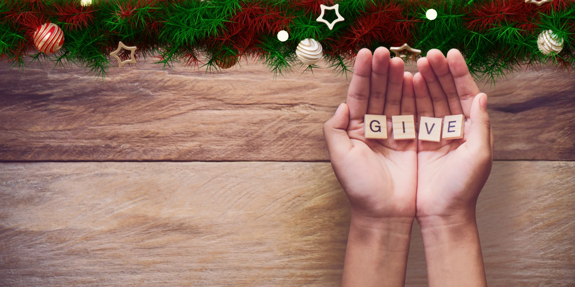 Hands holding tiles spelling "GIVE" with festive decorations and wooden background.